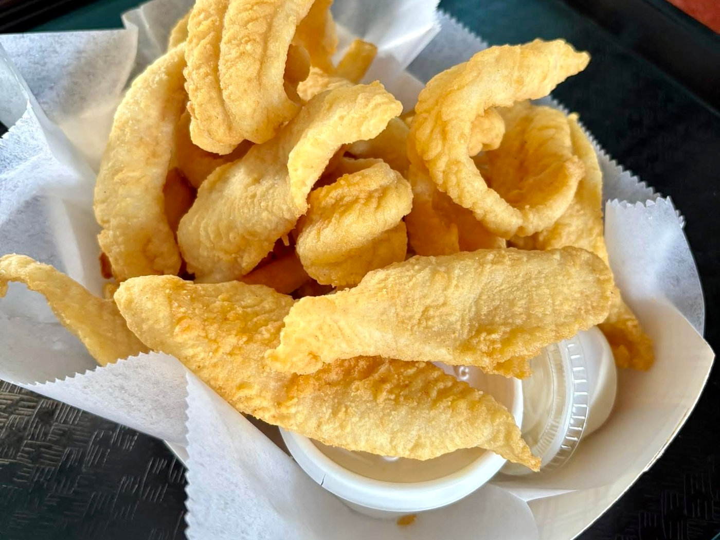 A basket of lightly breaded fried basa strips with a cup of tartar sauce