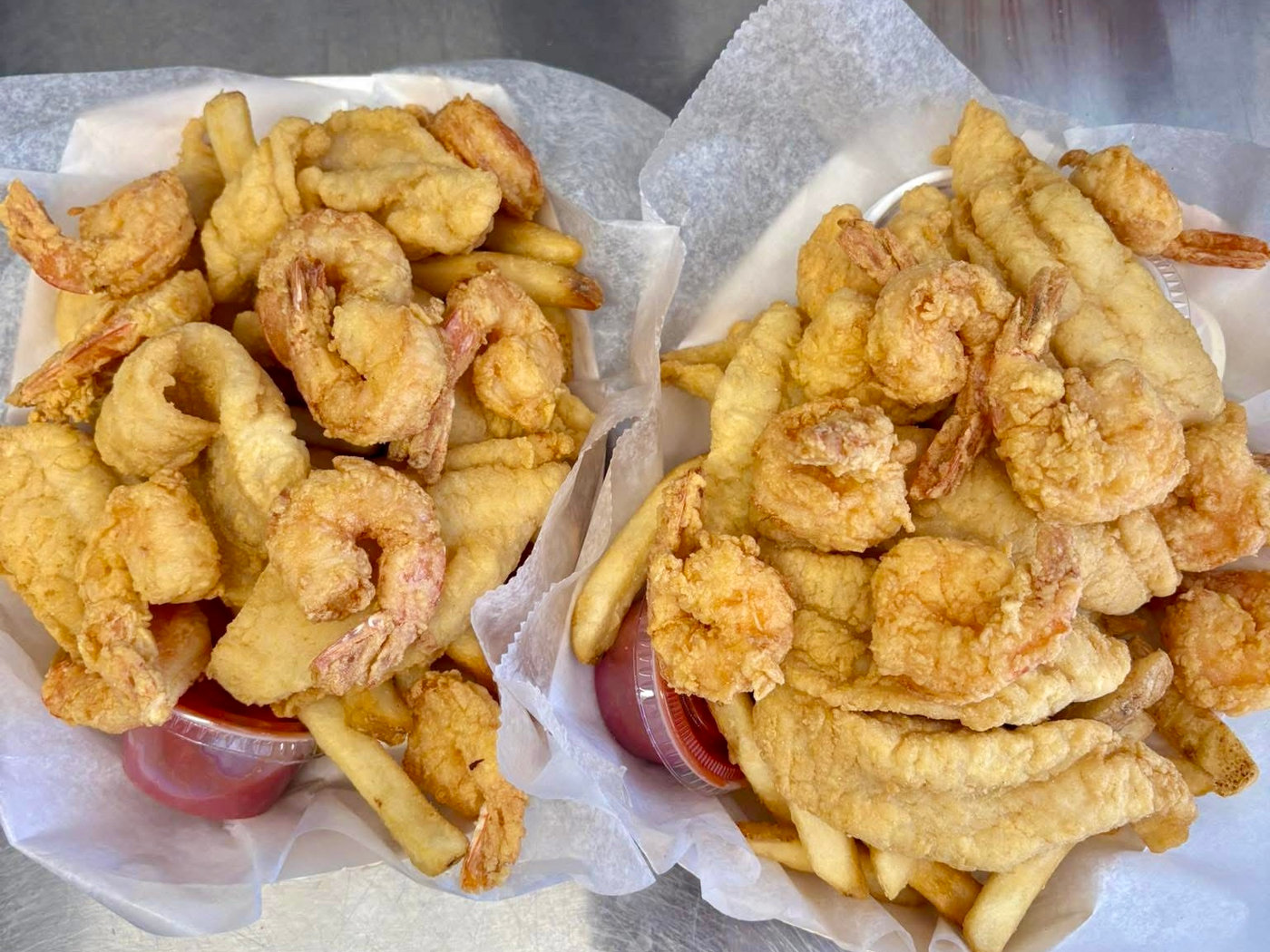 Two baskets of fried shrimp and fish strips served over french fries